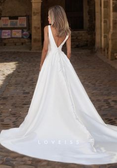 a woman in a white wedding dress standing on a cobblestone street with her back to the camera