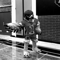 a mascot is standing on one foot in front of a brick wall and holding his arms out to the side