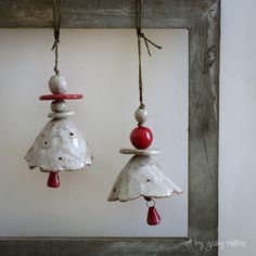 two ornaments hanging from strings on a wooden frame in the shape of bells with red and white beads