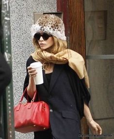 a woman walking down the street carrying a red purse and a coffee in her hand