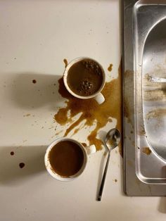 two cups of coffee sit in front of a dirty sink with rust on the floor