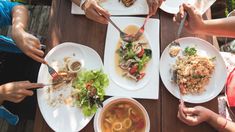 several people are sitting at a table with plates and bowls of food in front of them