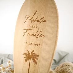 a wooden surfboard with a palm tree engraved on the front and bottom, sitting on a bed