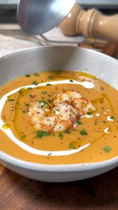 a white bowl filled with soup and shrimp on top of a wooden table next to a spoon