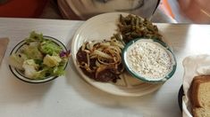 a white plate topped with food next to a bowl of beans and coleslaw