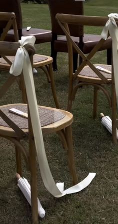 two wooden chairs with white ribbons tied around the back of them, sitting on grass