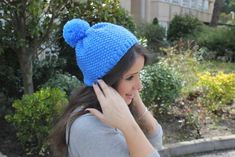 a woman wearing a blue knitted pom - pom hat while talking on her cell phone