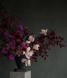 a black vase filled with lots of purple and white flowers on top of a table