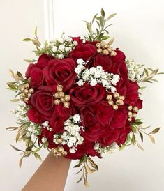 a bouquet of red roses and white baby's breath is held by a hand