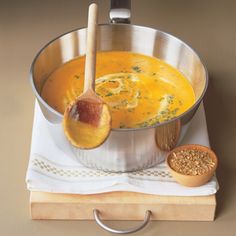 a metal pot filled with soup next to a wooden spoon on top of a table