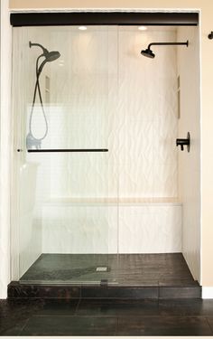 a bathroom with a glass shower door and black tile flooring on the side walk in shower