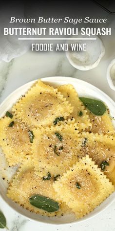 a white plate topped with ravioli and wine next to a bowl of pasta sauce