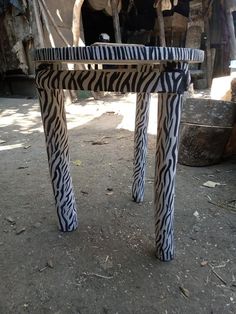 a zebra print table sitting on top of a dirt ground next to a cow in the background