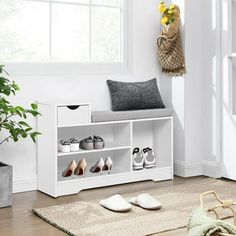 a white shoe rack with shoes and slippers next to a potted plant on the floor