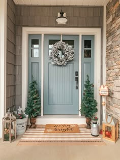 a blue front door with two christmas trees on the side and a welcome mat in front