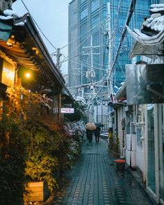 two people walking down an alley in the rain with umbrellas over their heads and buildings behind them