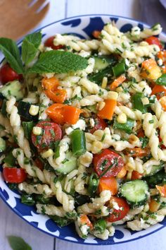 a pasta salad with tomatoes, cucumbers, and mint in a blue and white bowl