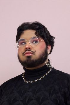 a man with glasses and a beard wearing a black shirt is standing in front of a pink wall