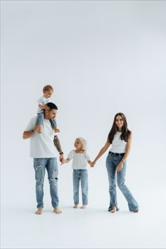 a family holding hands while standing in front of a white background with one child on his shoulders