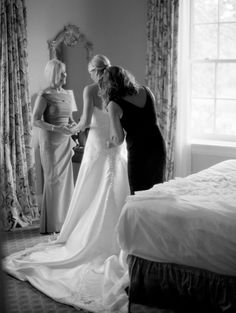 two women standing in front of a bed looking at each other's wedding dress