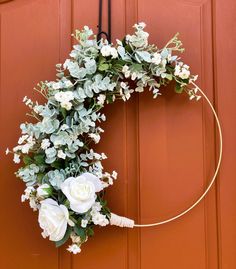 a wreath with white flowers and greenery hanging on a door