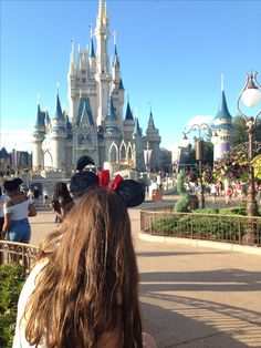 the back of a woman's head in front of a castle at disney world