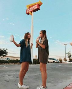 two girls standing in front of a taco bell sign and holding up their mugs