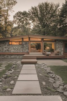 a modern house with stone walls and steps leading to the front door, surrounded by trees