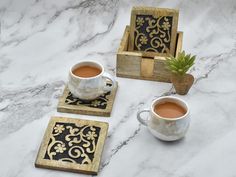 two cups of tea sit on coasters next to a potted plant