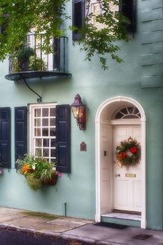 a blue building with shutters and flowers in the window boxes on the front door