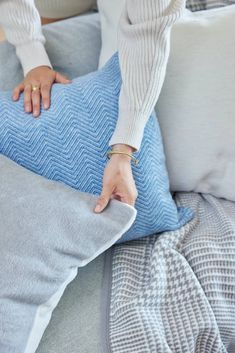 a woman holding onto a blue pillow on top of a gray couch with white pillows