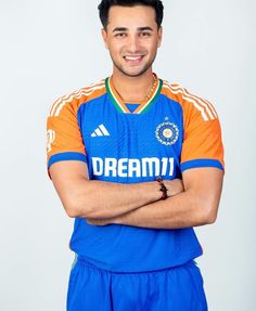 a man with his arms crossed standing in front of a white background wearing a blue and orange jersey