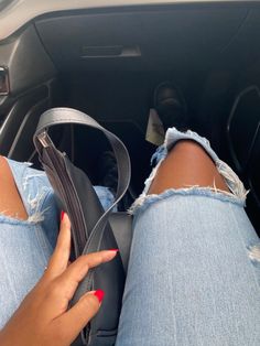 a woman with red nails sitting in the drivers seat of a car holding her purse