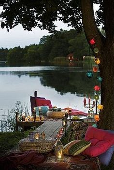 an outdoor seating area next to a lake with lights strung from the trees and lanterns