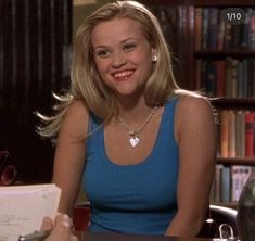 a woman sitting at a table with a book in front of her and holding a pen