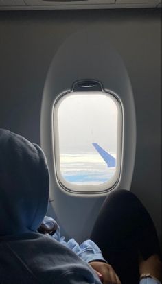 an airplane window looking out at the ocean and sky with a person laying down in bed