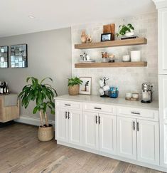 a kitchen with white cabinets and wooden shelves filled with pots, plants and other items