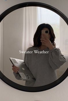 a woman taking a selfie in front of a mirror with the words sweater weather on it