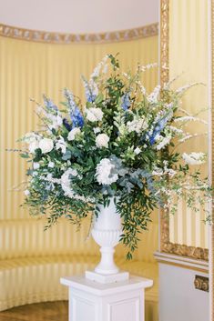 a vase filled with white and blue flowers sitting on top of a table next to a mirror