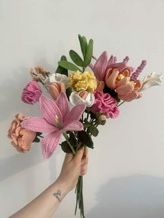 a person is holding a bouquet of flowers in their hand, against a white wall