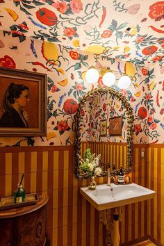 A busy and beautiful room features tan and yellow vertical stripes of cement tile, while a bold floral wallpaper, painting of a woman, and a leaf mirror over a sink complete the space. Maximalism Interior, Zia Tile, More Is More, Bathroom Wallpaper, House Bathroom, La Jolla, Design Firms