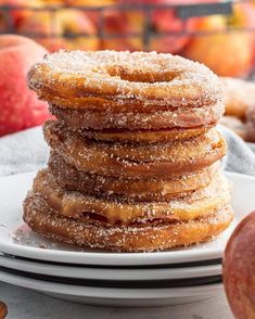 a stack of donuts sitting on top of a white plate next to an apple