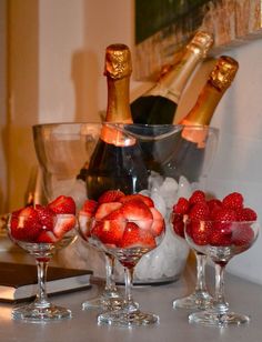 three wine glasses with strawberries in them and two champagne bottles on the counter top