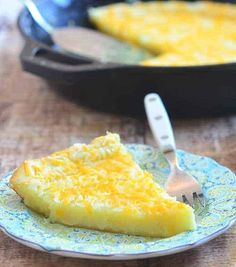 a slice of cheese cake on a plate with a fork and skillet in the background