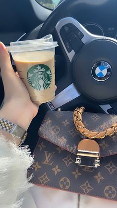 a woman holding a cup of coffee in her hand while sitting in the drivers seat of a car