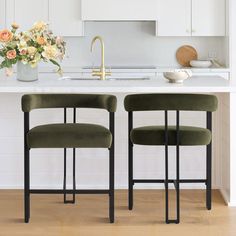 two green chairs sitting in front of a white kitchen island with flowers on the counter