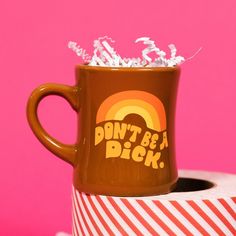 On a hot pink background sits a mug with white crinkle and big, colorful confetti scattered around. The mug is a brown diner style mug with orange, groovy style font that says Don't Be A Dick. with an orange, light orange and yellow rainbow above it. It has white crinkle in it and sits atop a red and white striped roll of tape. Retro Quotes, Candle Cards, Funny Coffee Mug, Kids Bath, Warm Hug, Birthday Thank You, Funny Coffee, Funny Coffee Mugs, Coffee Humor