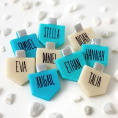 small personalized name tags with silver glitter accents on blue and white paper, surrounded by rocks