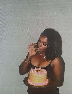 a woman holding a cell phone to her mouth while standing in front of a cake