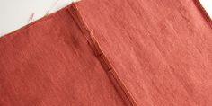 an orange piece of cloth is laying on top of a white surface with red thread